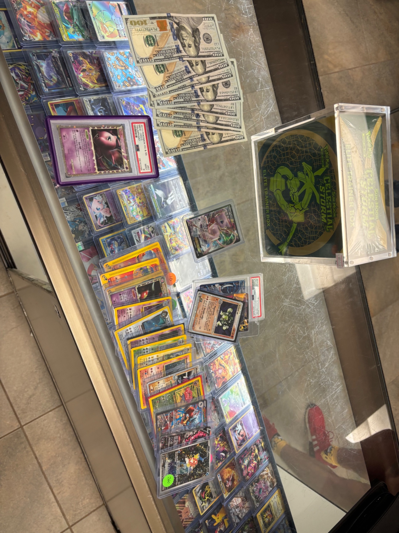 Glass display case with PSA Shining Mew, vintage singles, cash, and a sealed Celestial Storm Elite Trainer Box