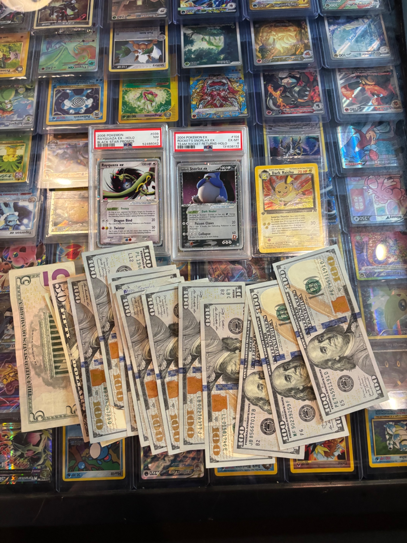 Cash payout fanned over a display case full of vintage PSA Pokémon slabs